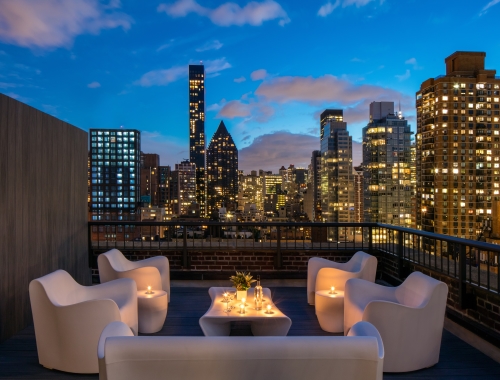 luxurious chairs with candles on the penthouse rooftop terrace at AKA Sutton Place with beautiful buildings in the background lit up