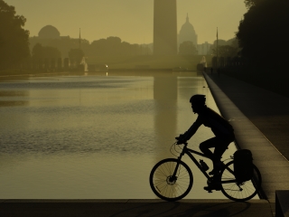 A Man Riding A Bicycle Next To A Body Of Water