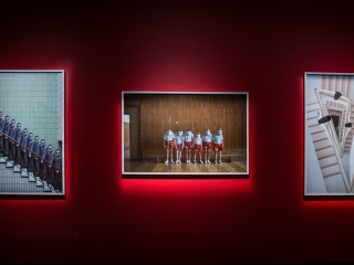 A Group Of People Standing In A Room With A Red Wall